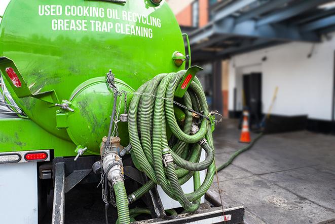 a professional plumber using a pump to empty a grease trap in Allston, MA